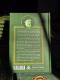 Back cover of a green Islamic book featuring a scholar's portrait, gold border, and descriptive text about Shia literature.