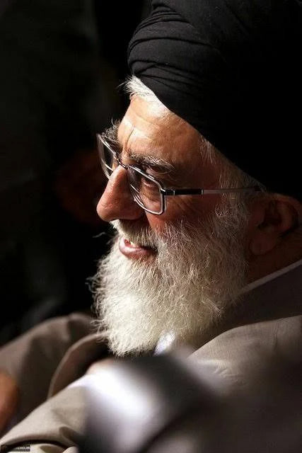 Elderly man with white beard, glasses, and black turban, wearing traditional Islamic clothing.