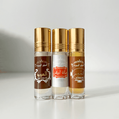 Three glass perfume bottles with gold caps labeled Al Oud, Musk Blanc, and Anbar on white background.